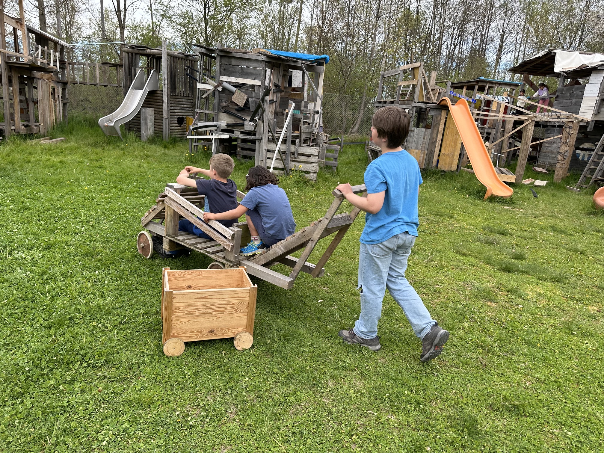 Kinder mit einem selbstgebauten Holzwagen auf dem Bauspielplatz
